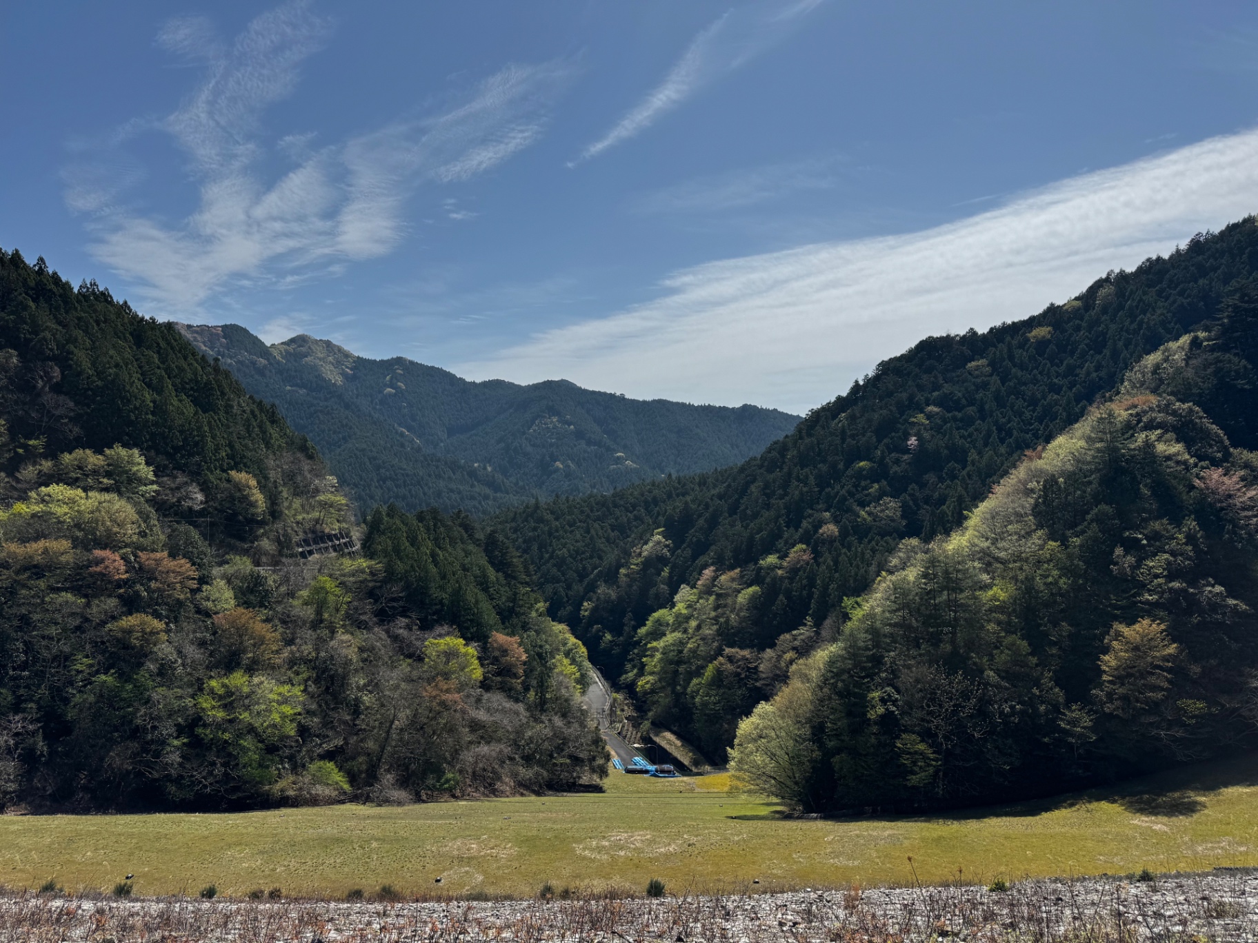 Weites Bergtal in Japan mit Waldhängen, offener Wiese und feinen Wolkenschleiern am Himmel