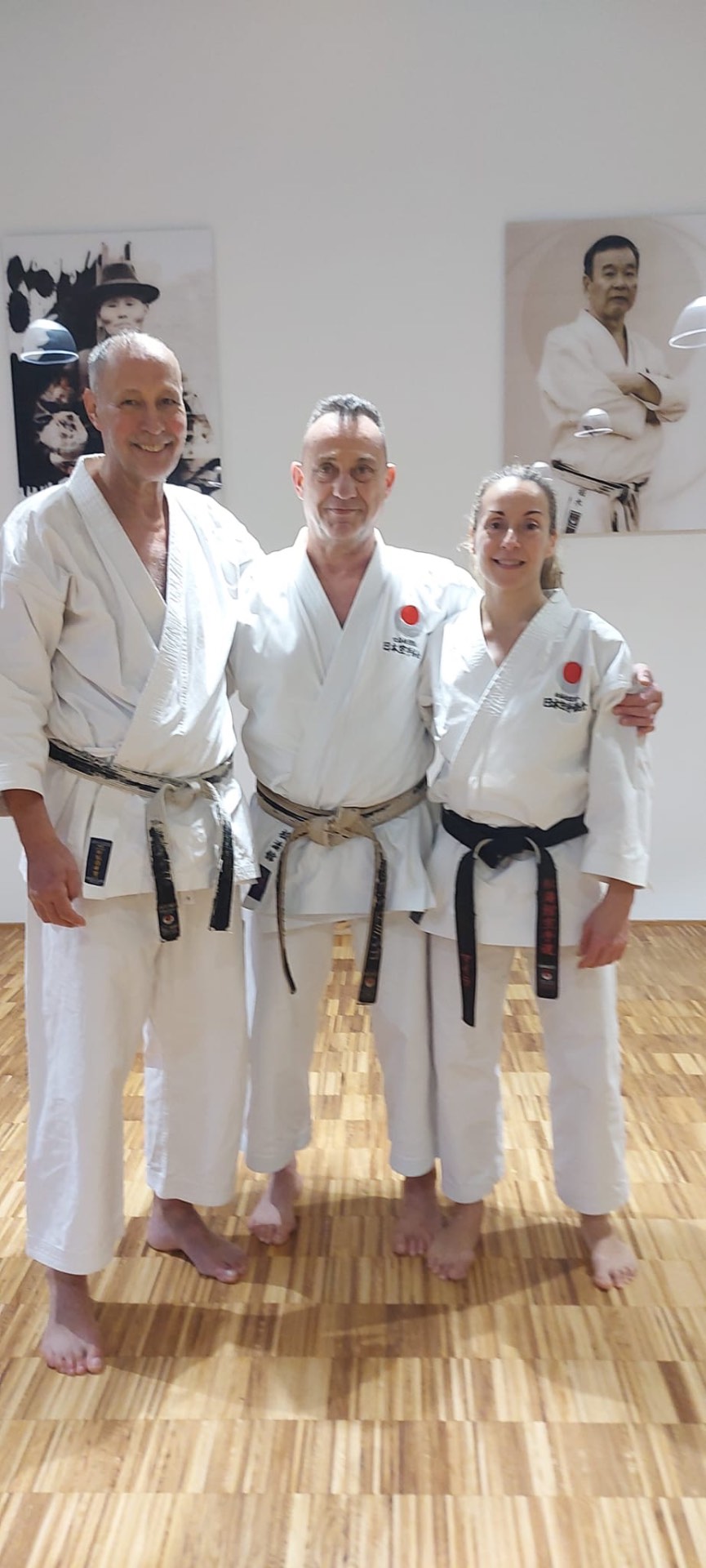 Drei Schwarzgurte im Dojo vor den Porträts der JKA-Meister