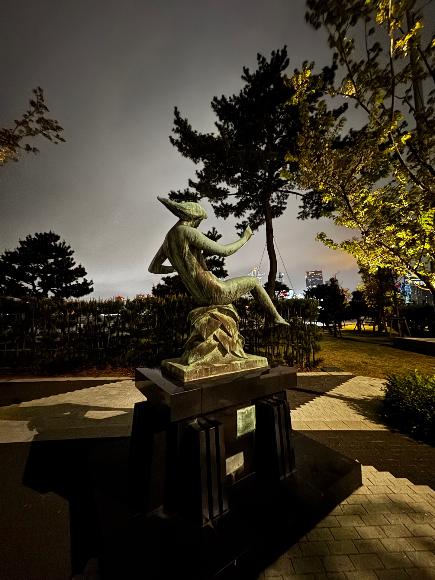 Bronzestatue in einem Park bei Nacht mit Blick auf die Skyline von Yokohama